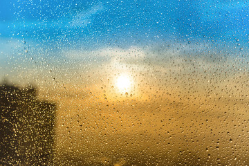 Beautiful sunset through a spattered glass with water rain drops and building silhouette