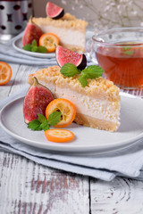 Piece of grated pie with cottage cheese topped with figs and kumquats on ceramic plate on white wooden table
