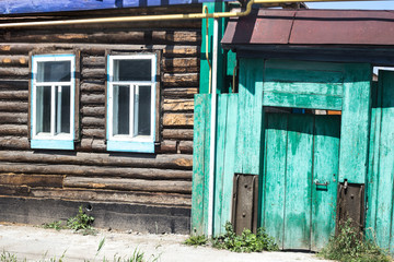 facade of an old log building with two windows and a green fence in a remote village
