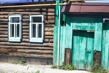 Fototapeta na wymiar facade of an old log building with two windows and a green fence in a remote village