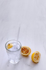 Glass of water with lemon and squeezed lemons on a wooden table.