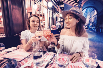 Two mixed race girls friends clinking glasses while enjoying an celebrating moment in cafe at evening time