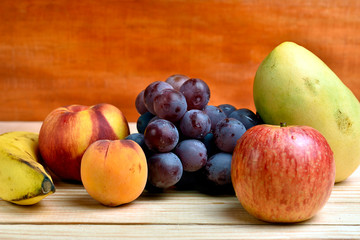 Seasonal fruits, peach, mango, apple, banana grapes, placed on a wooden base and diffuse background