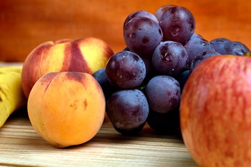 Seasonal fruits, peach, mango, apple, banana grapes, placed on a wooden base and diffuse background