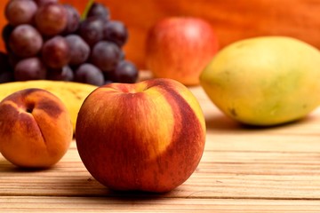Obraz na płótnie Canvas Seasonal fruits, peach, mango, apple, banana grapes, placed on a wooden base and diffuse background