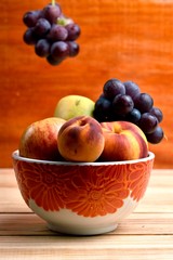 Seasonal fruits, grapes, mango, apple, peach, placed in a plastic bold sibre a wooden table and a diffuse background of orange wood