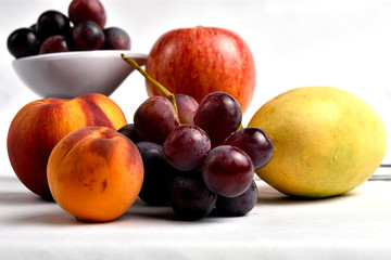 Seasonal fruits in which peach, grapes, apple and mango are placed, placed on a white tablecloth, white diffuse background