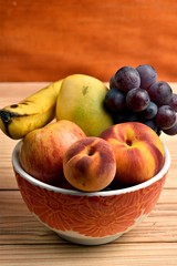 Seasonal fruits, grapes, mango, apple, peach, placed in a plastic bold sibre a wooden table and a diffuse background with and orange wood