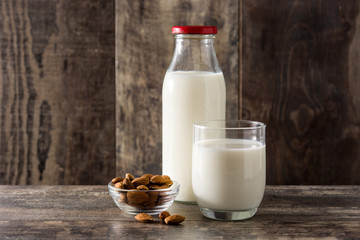 Almond milk in glass and bottle on wooden table. 