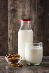 Almond milk in glass and bottle on wooden table. 