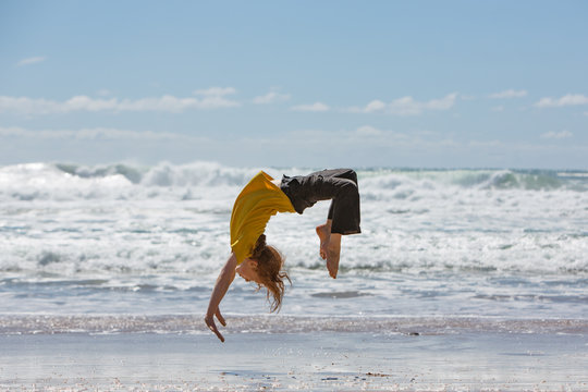 A redheaded boy back-flipping on a beach