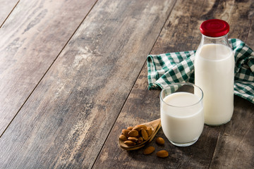 Almond milk in glass and bottle on wooden table. Copy space