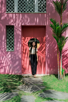 Beautiful girl posing against the pink wall with tree shadows