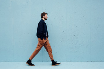 Stylish man walking against the blue wall background