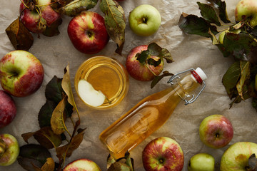 top view of bottle and glass with cider near apples and branch with leaves