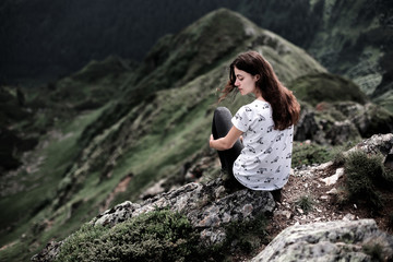 Naklejka na ściany i meble Rear view of a young woman sitting on a mountain top. Woman hiking around mountains