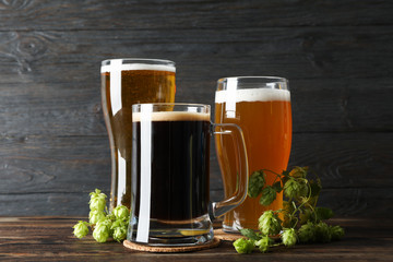 Different mugs with beer and hop cones on wooden table, copy space
