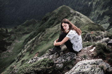 Young woman sitting on a mountain top. Woman hiking around mountains. Calm and inspiration on high peak of mountain