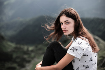 Portrait of young girl sitting on a mountain top. Woman hiking around mountains. Calm and inspiration on high peak of mountain