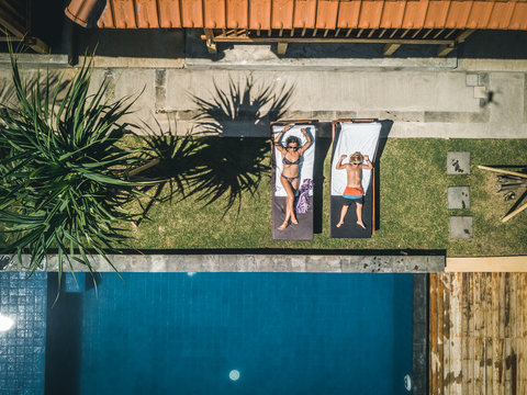 drone shot of a mother and son relaxing on sun loungers in tropical resort at the pool