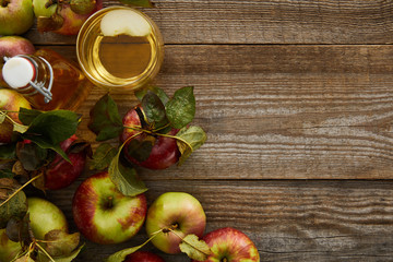 top view of ripe apples near bottle and glass of fresh cider on wooden surface