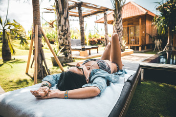 beauty in denim shirt, bikin and sunglasses listening to music on a sun lounger from above