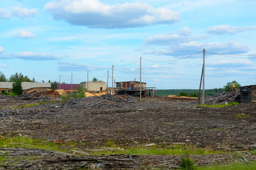 An old building with a strangely sagging roof near an abandoned sawmill field and sheds in a village in Northern Yakutia.