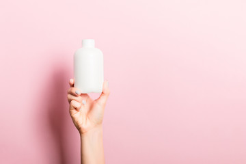 Female hand holding cream bottle of lotion isolated. Girl give tube cosmetic products on pink background