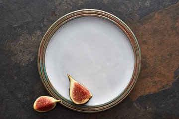 top view of ripe cut delicious figs on round white plate on stone background