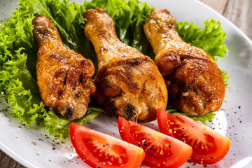 Fried chicken drumsticks with vegetables on wooden table