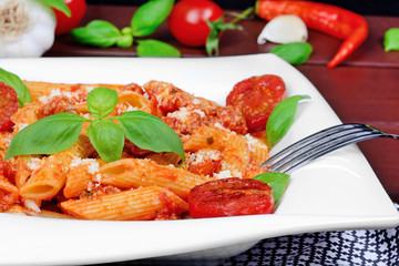 Penne with tomatoes sauce and parmesan in a plate on table