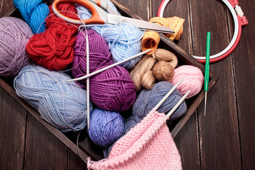 Multi-colored yarns of thread for knitting, knitting needles, hook in a wooden box on a brown background