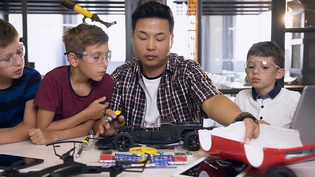 Portrait of three boys with teacher of electronics engineer using screwdriver to disassemble robotic machine at the table in the modern school