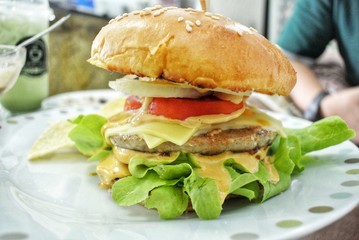 Hamburger with vegetables, cheese and potato chips on a vintage style wooden table