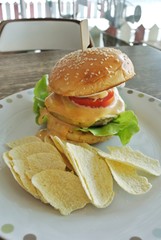 Hamburger with vegetables, cheese and potato chips on a vintage style wooden table
