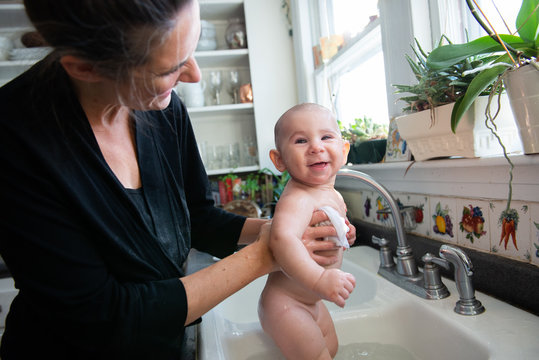 Mother Gives Baby a Bath in the Kitchen Sink