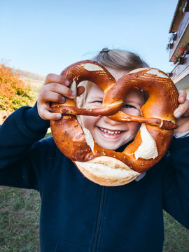 People: Young smiling girl holding a pretzel in front of her face