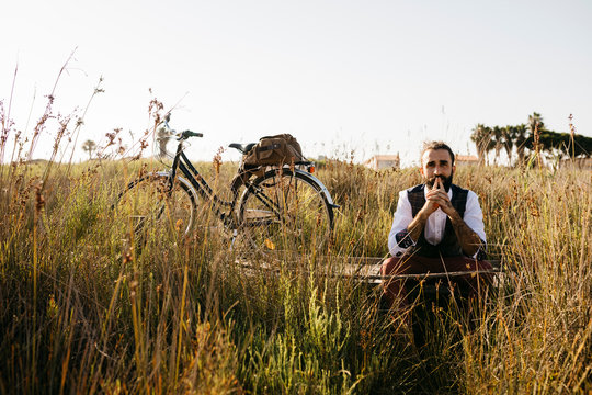 Well dressed man sitting on a wooden walkway in the countryside next to a bike