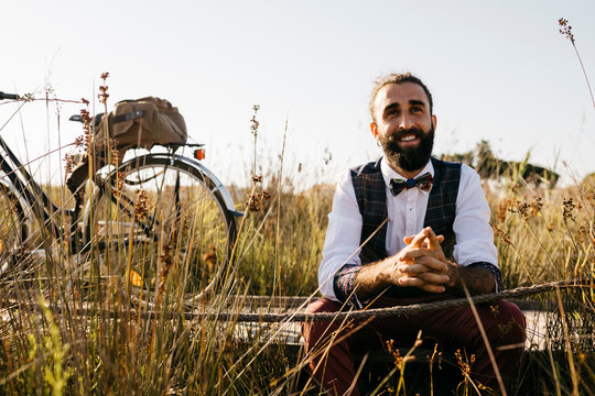 Well dressed man sitting on a wooden walkway in the countryside next to a bike