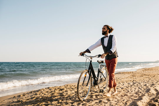 Well dressed man walking with his bike on a beach