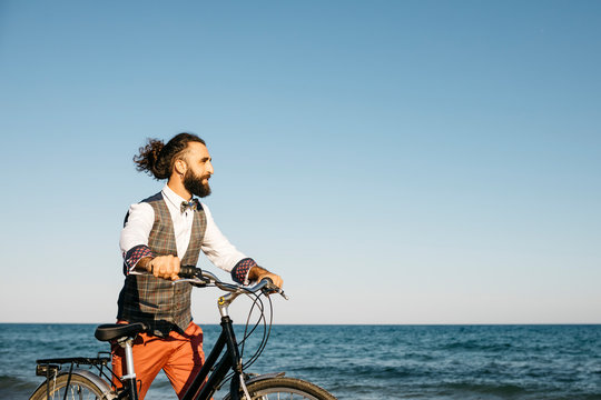 Well dressed man walking with his bike on a beach