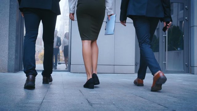 Feet of three business people commuting to work. Businessmen and businesswoman go to office building. Rear back view of Colleagues going in the city outdoor.