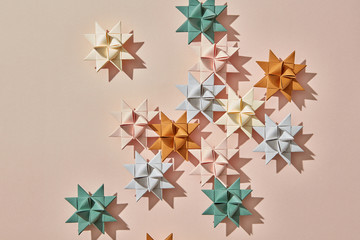 Handcraft colorful origami stars on a light brown background with reflection of shadows and copy space. Flat lay