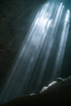 Girl stands under the rays of light in a deep cave Jomblang Cave. Java, Indonesia