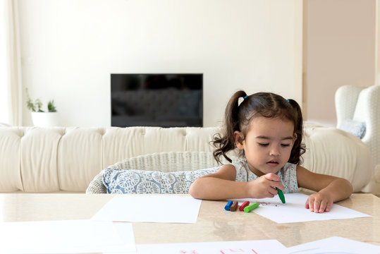 Litlle girl drawing with color waxes at home