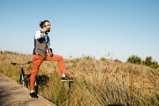 Well dressed man standing on a wooden walkway in the countryside talking on cell phone