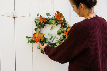 young woman hanging a fall wreath on a barn door