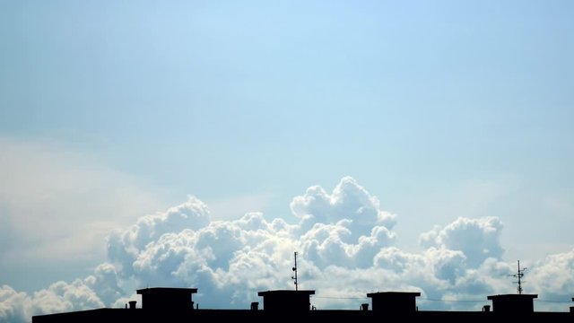 Slow movement of massive clouds in the distance on the blue sky. Framed by the silhouette of the house roof with 4 small elevator machine rooms.