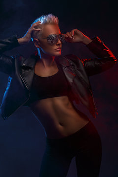 Portrait of a stylish attractive girl with short blond hair in sunglasses on a dark background. Creative color. Studio photography.