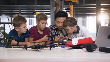 Teacher of electronic engineer together with caucasian students working with model of car robot